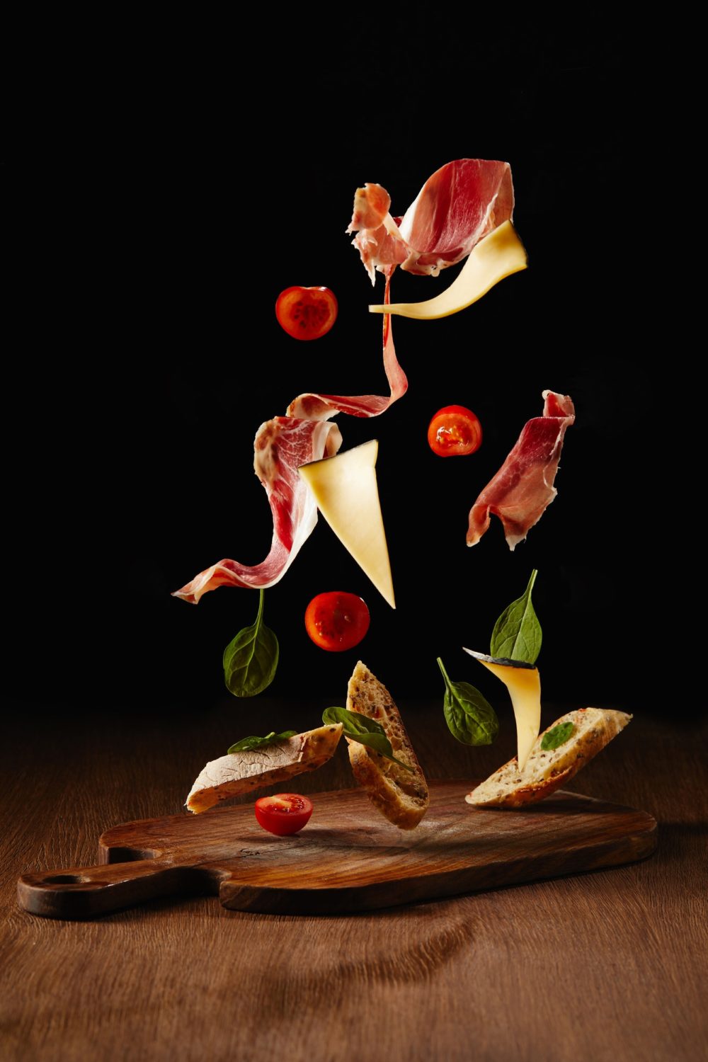 Ingredients for snack with bread, jamon and vegetables flying above wooden table surface