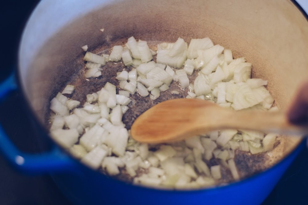 Onions are sautéing in a blue iron pot, Dutch oven, on a stovetop