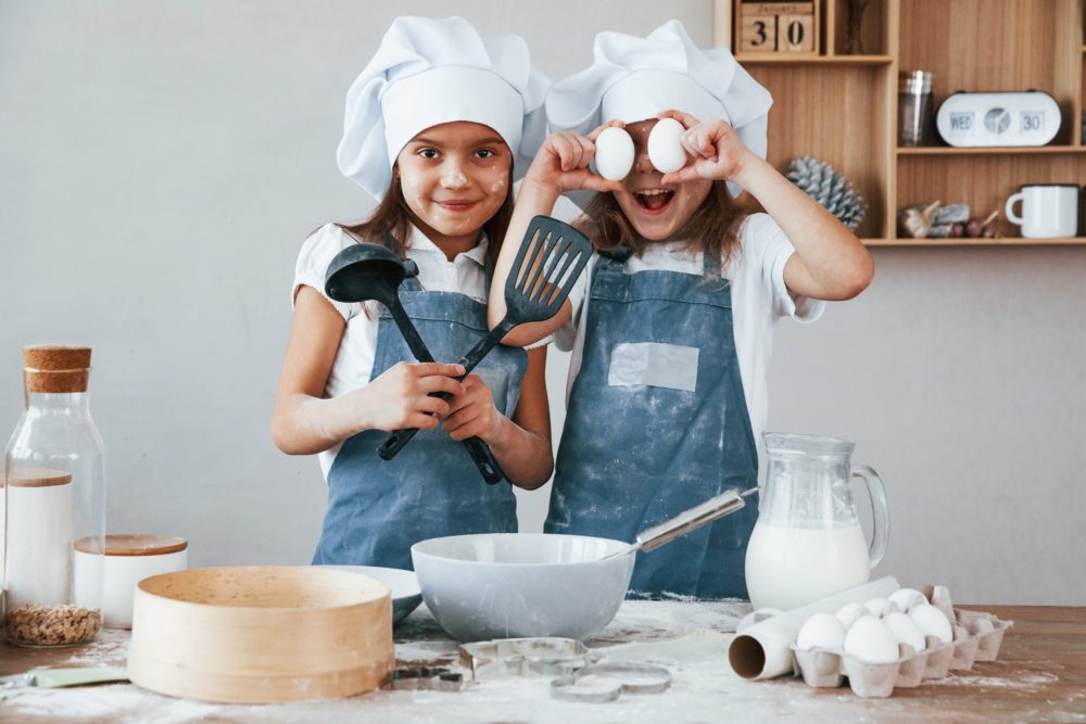 Two little girls in blue chef uniform have fun while preparing food on the kitchen
