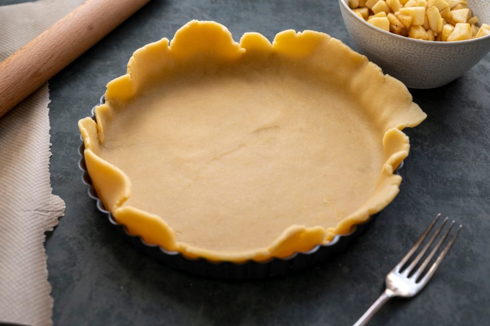 Homemade pie crust in pie plate. Cooking apple pie, dark background