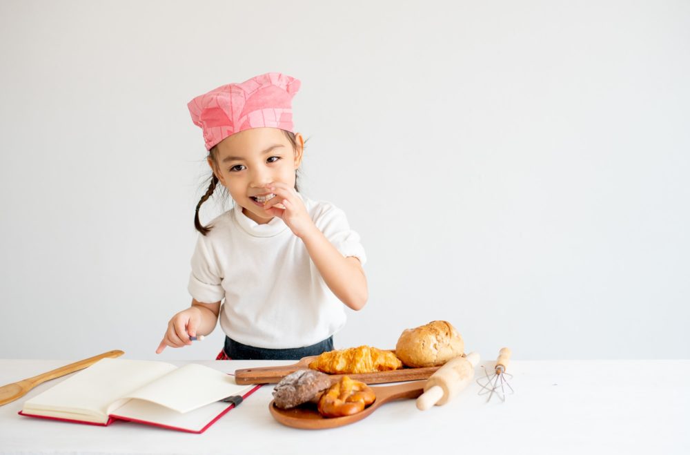 Asian little chef girl test the taste of bread on the table by pick some piece and eat