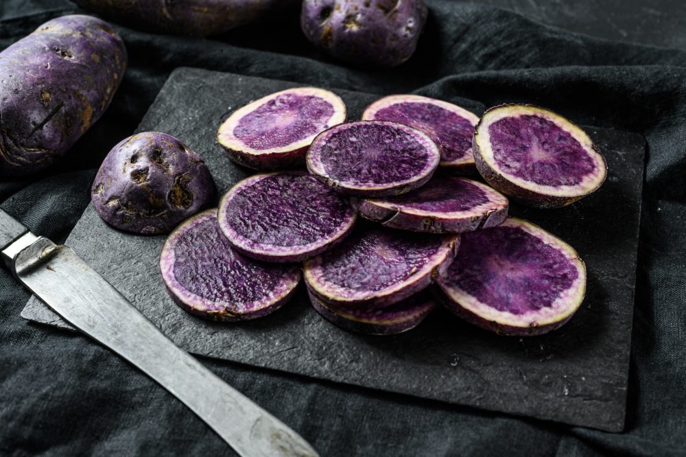 Raw sliced violet potatoes. Black background. Top view