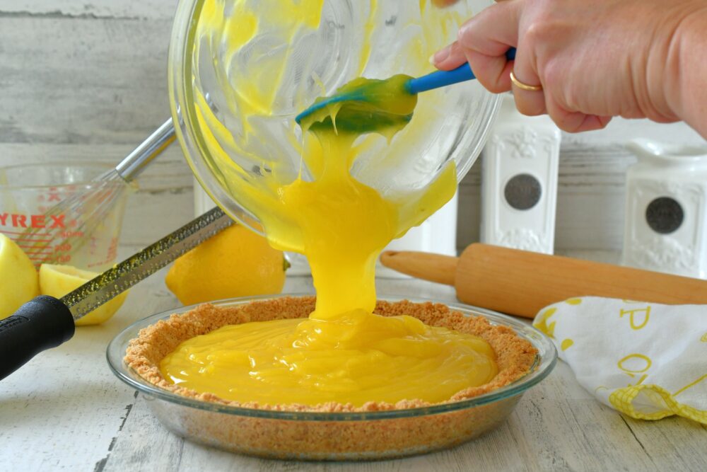 Pouring homemade lemon pie filling into graham cracker crust for a lemon meringue pie in the kitchen