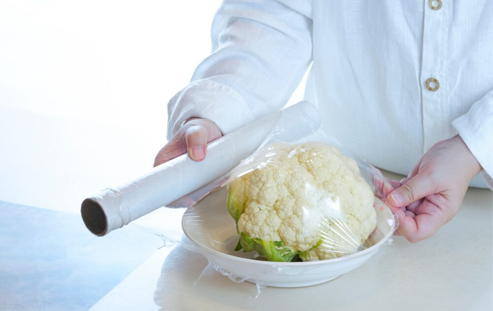 Close up of woman hand using food film wrapping organic cauliflower on table in the kitchen