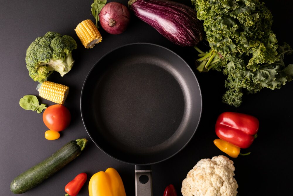 Overhead view of empty frying pan amidst various vegetables on black background